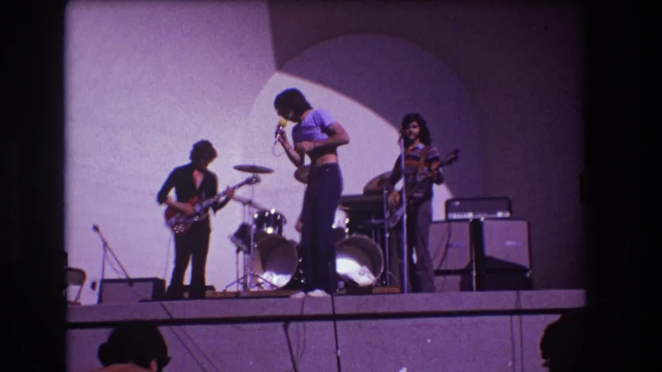 The closing 1973 Medford frame shows the singer leaning toward the microphone while the guitarist, bassist, drums, and amplifiers fill the stage.