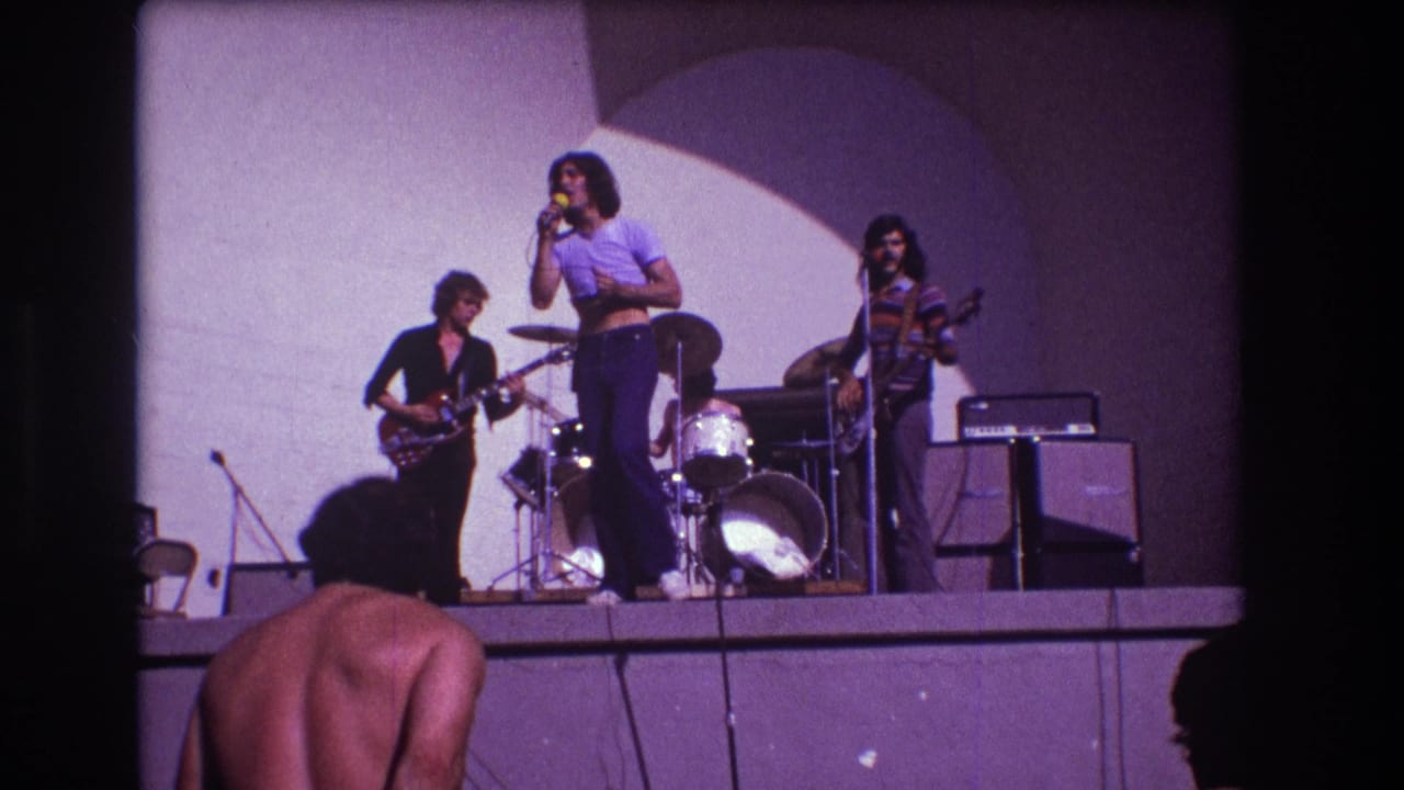 1973 Medford, New Jersey 8mm frame with a rock band onstage and a shirtless audience member partly visible in the foreground.
