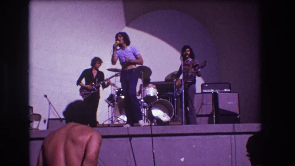 1973 Medford, New Jersey 8mm frame with a rock band onstage and a shirtless audience member partly visible in the foreground.