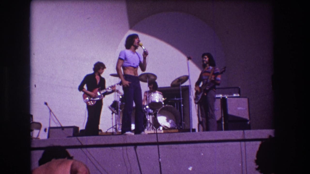 1973 Medford, New Jersey concert frame showing the singer at center with guitarist, bassist, drummer, microphones, and amplifiers around him.