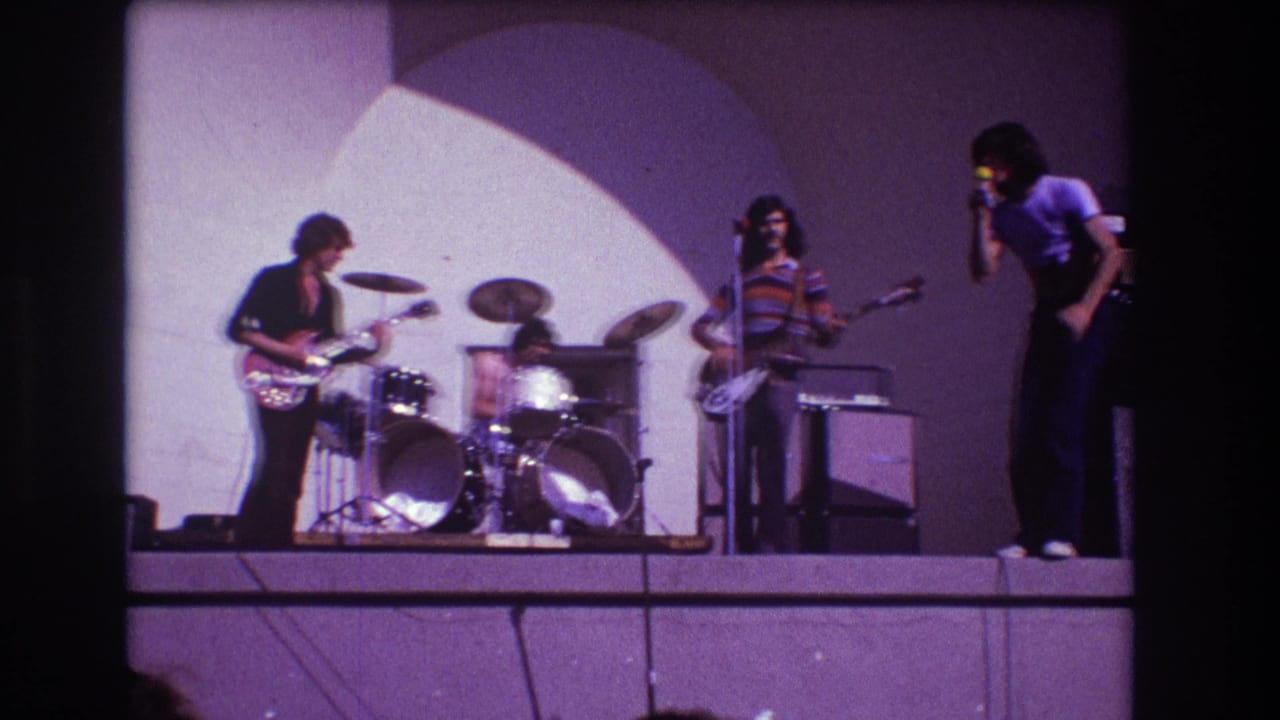 Four-piece rock band on a small stage with guitarist, drummer, bassist, and singer.