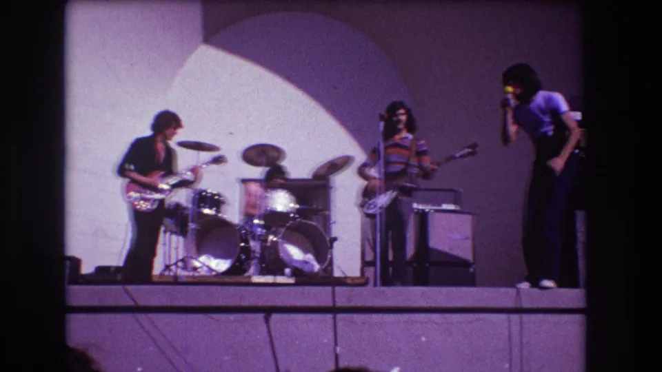 1973 Medford, New Jersey 8mm frame showing a rock band performing on stage under an arched spotlight.