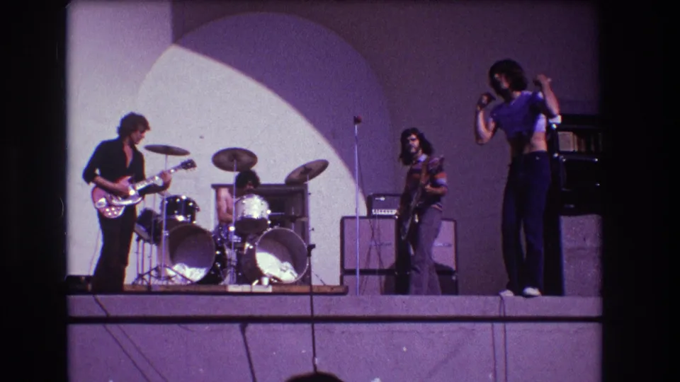 1973 Medford rock performance frame with the singer turned slightly away and the band spread across the lit stage.
