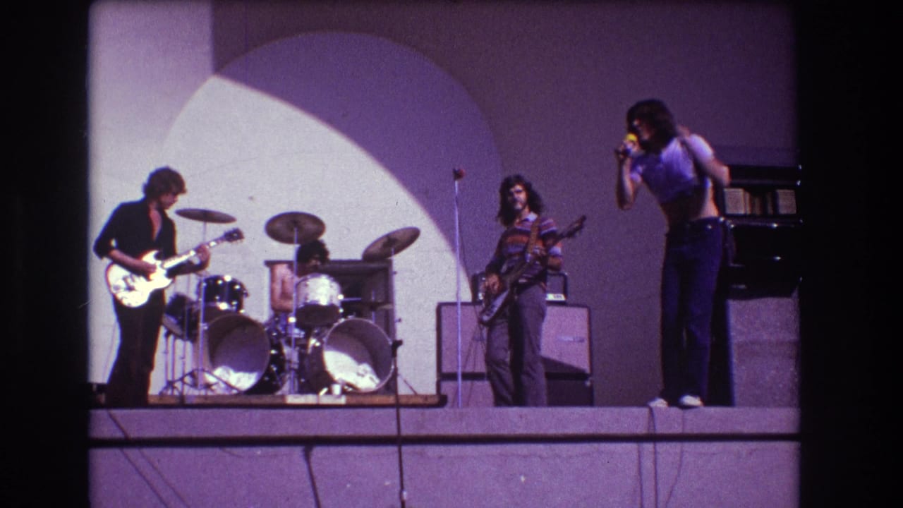 Four-piece rock band on an outdoor stage with singer, guitarist, bassist and drummer.