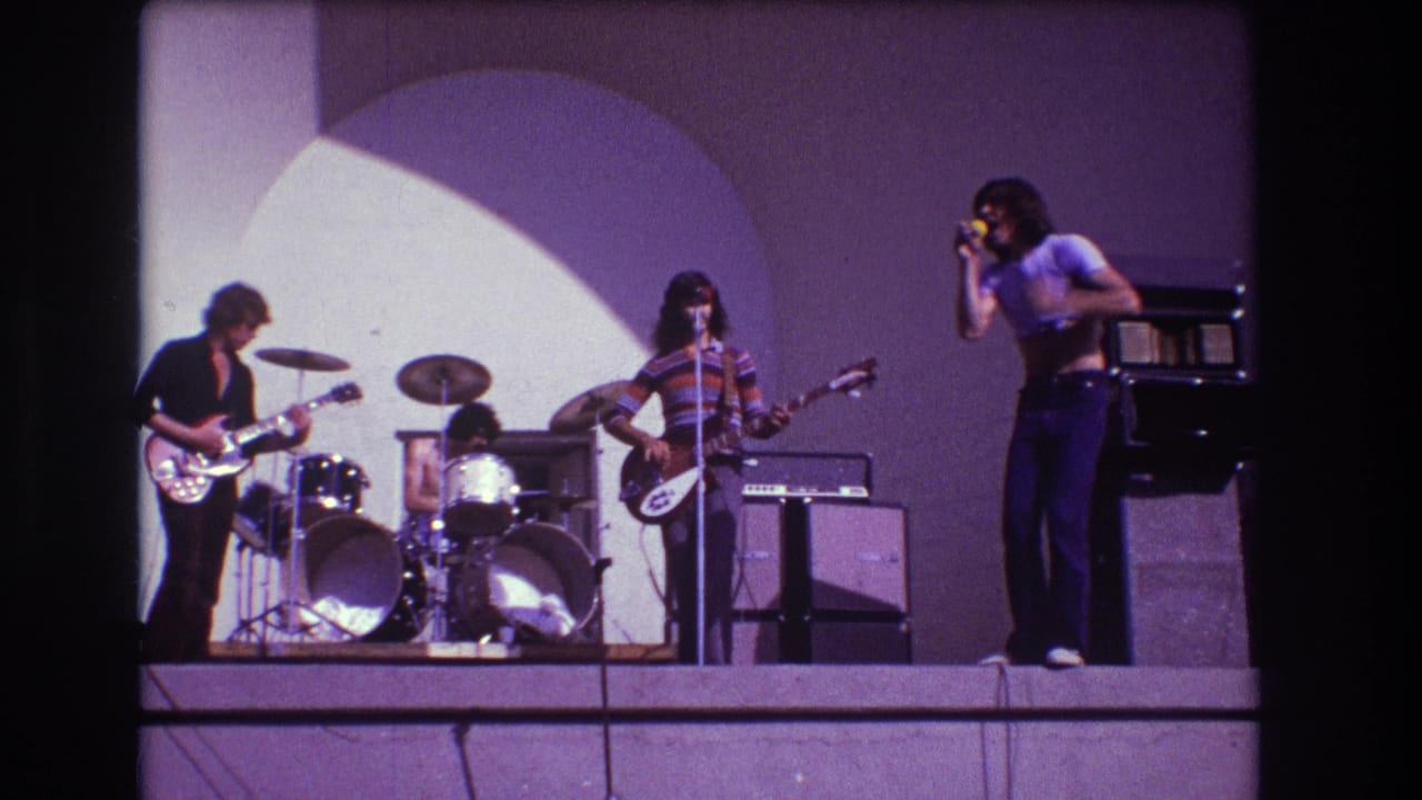 Band members play on stage while the singer leans into a handheld microphone.
