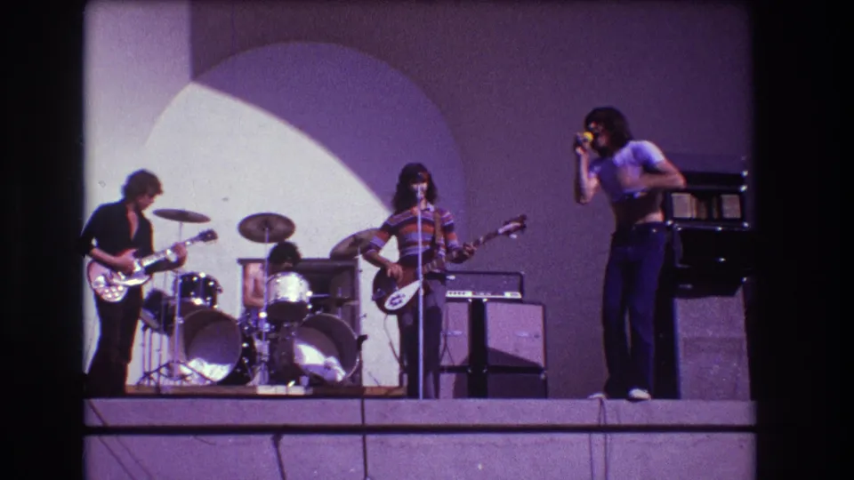 1973 Medford, New Jersey frame showing a rock singer at right with guitarist, bassist and drummer continuing the outdoor performance.