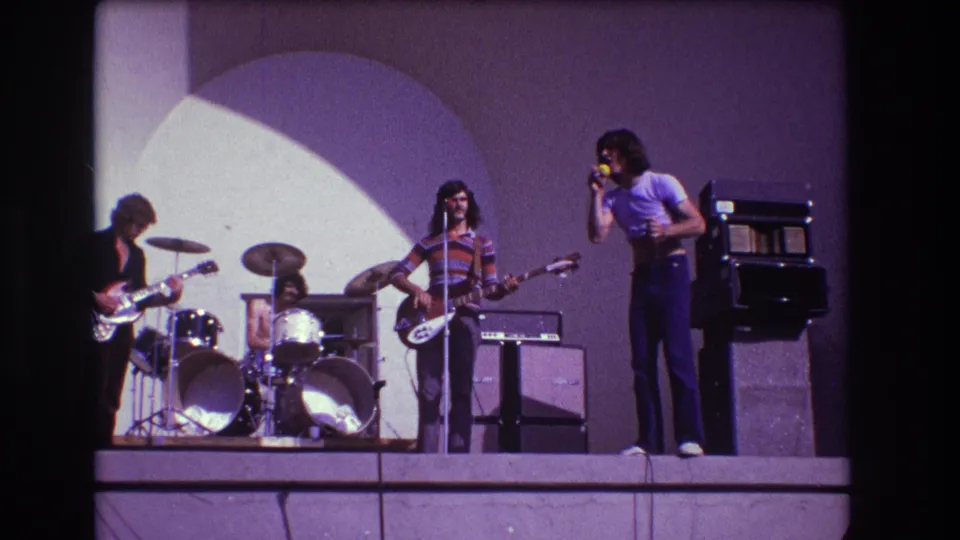 1973 Medford, New Jersey home-movie frame of the singer and three bandmates performing with drum kit, guitars and stage amps.