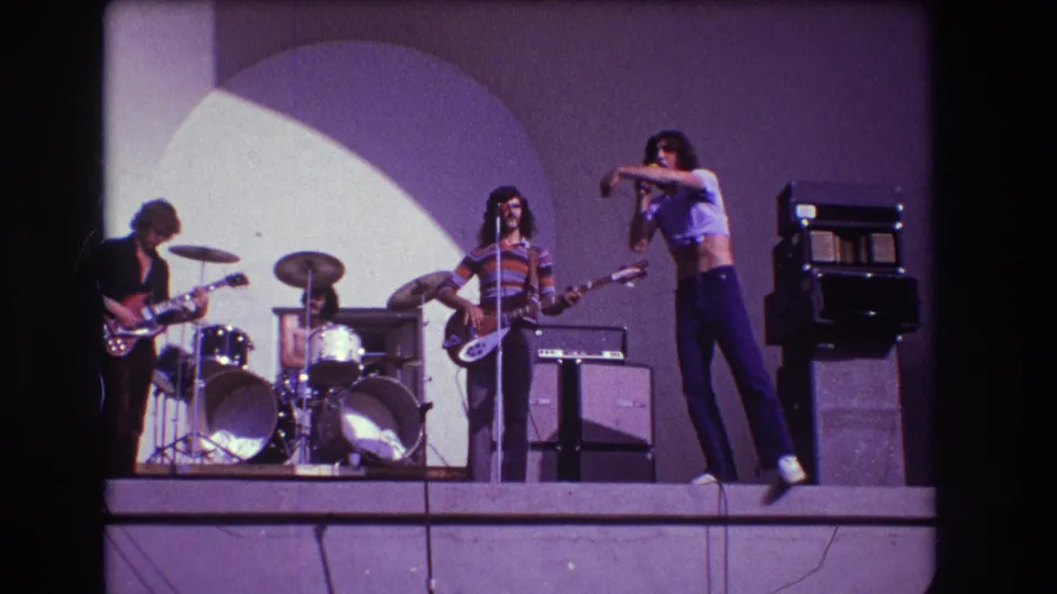 1973 Medford, New Jersey frame showing the singer gesturing beside the bassist, guitarist and drummer during an outdoor rock performance.