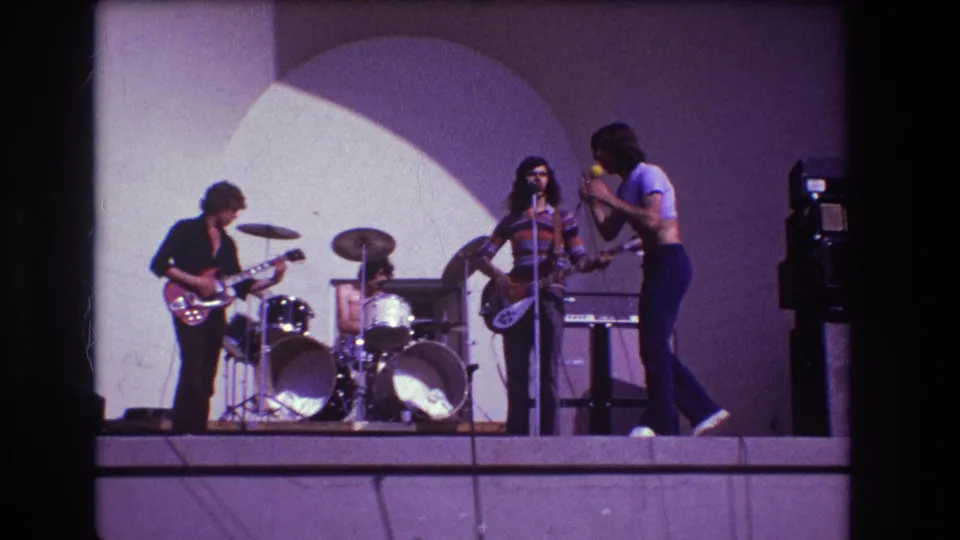 The final frame shows the 1973 Medford rock performance from the audience viewpoint, with the singer facing the bassist as the guitarist and drummer play.