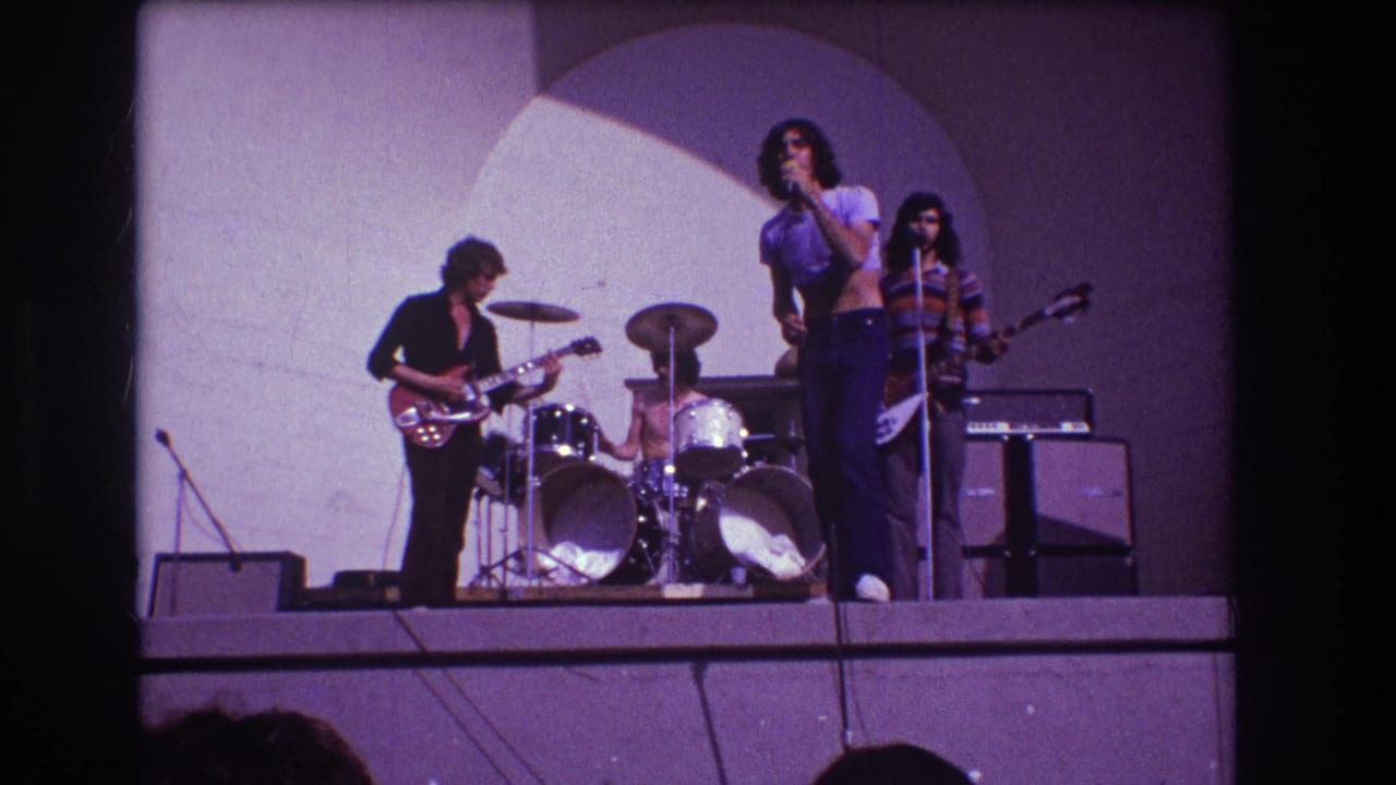 Rock band performing on a stage with singer, guitarist, drummer, bassist, and amplifiers visible.