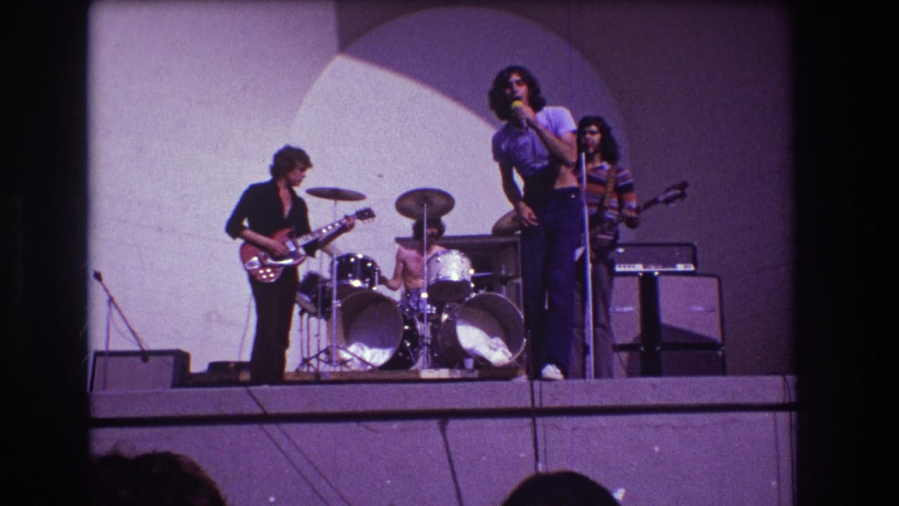 Singer at a microphone with guitarist, drummer, bassist, drum kit, and amplifiers on stage.