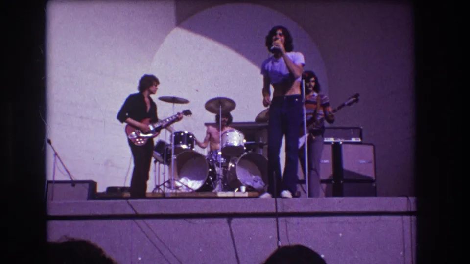 1973 Medford, New Jersey concert frame showing the singer centered in front of a small rock band with instruments and amps visible.