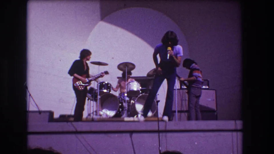 1973 Medford, New Jersey home-movie frame showing the singer bending forward during a rock performance as the band continues playing.