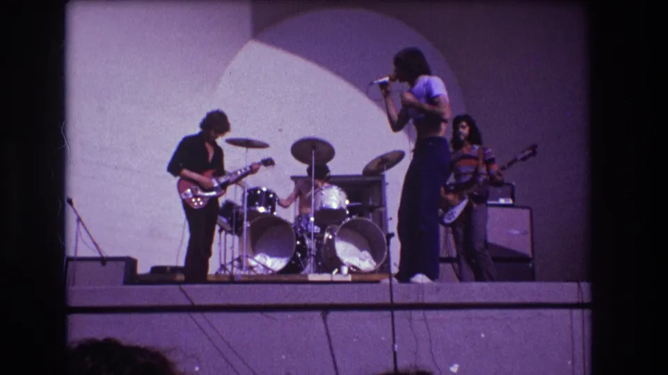 1973 Medford, New Jersey frame of a four-piece rock band performing outdoors, with visible instruments, amps, and film grain.