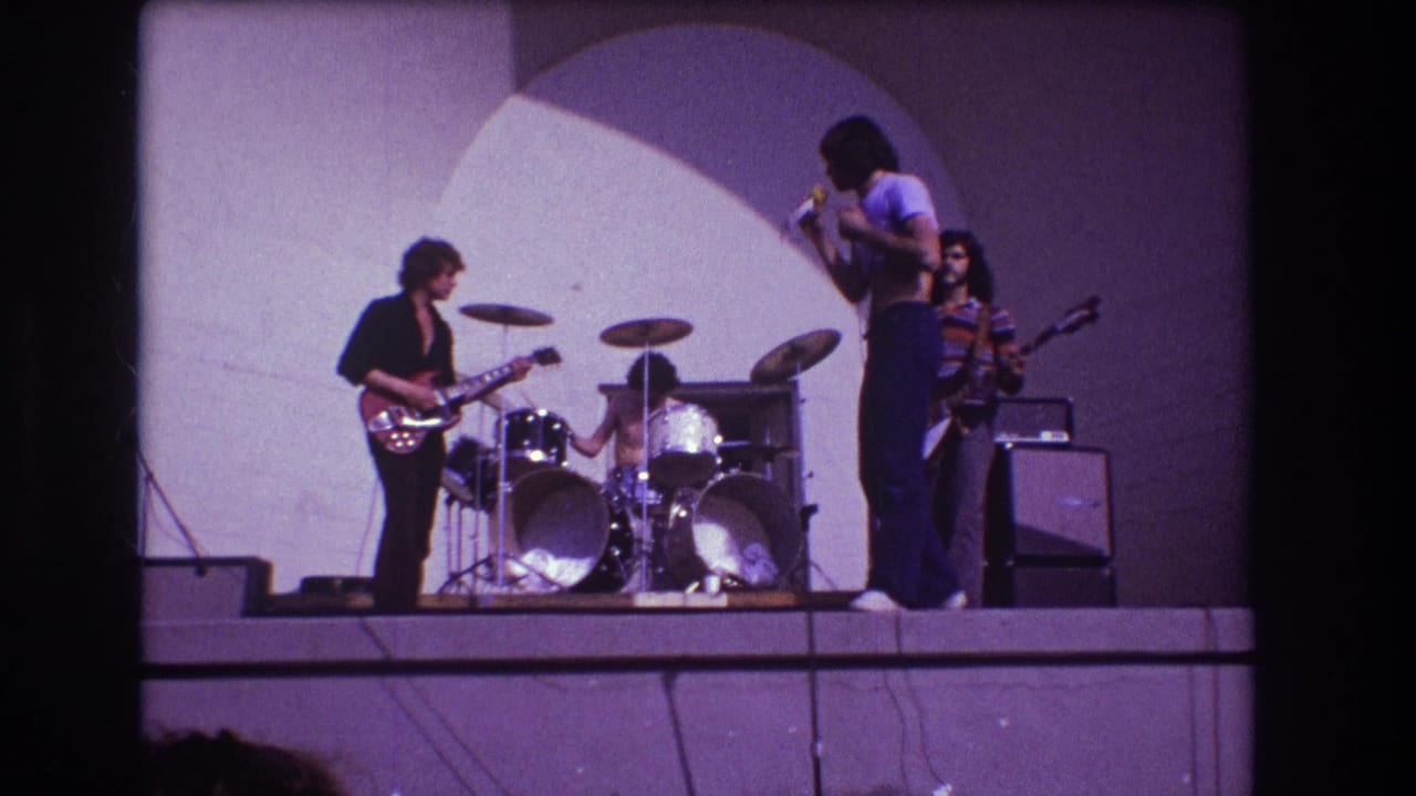 1973 Medford, New Jersey 8mm frame showing a Black male singer with microphone beside a guitarist, drummer, and bassist on an outdoor stage.