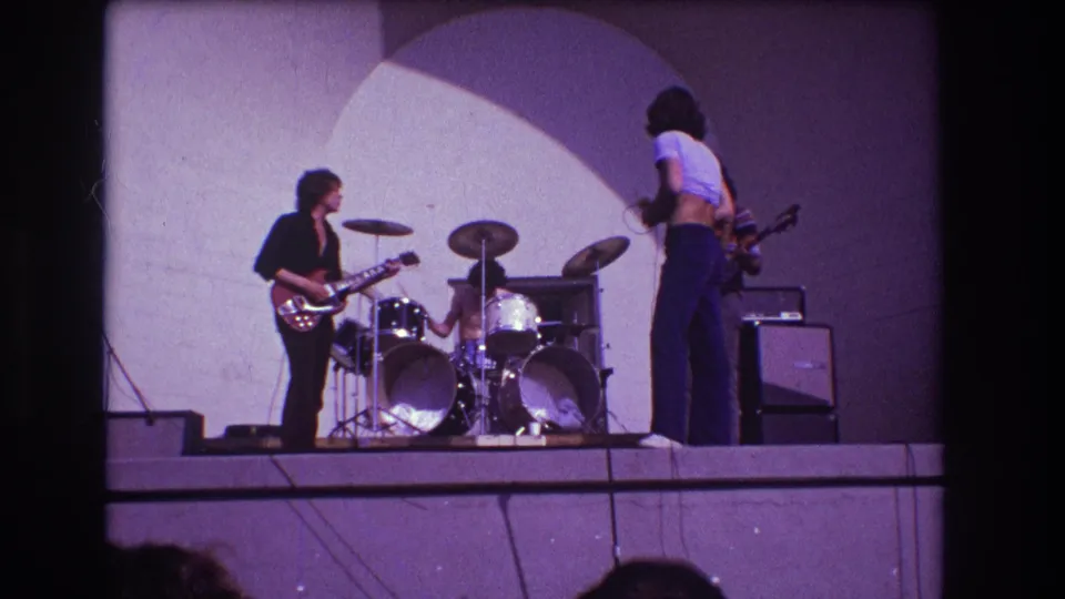 1973 Medford, New Jersey concert frame with the singer turned partly away from camera as the guitarist and drummer continue on stage.