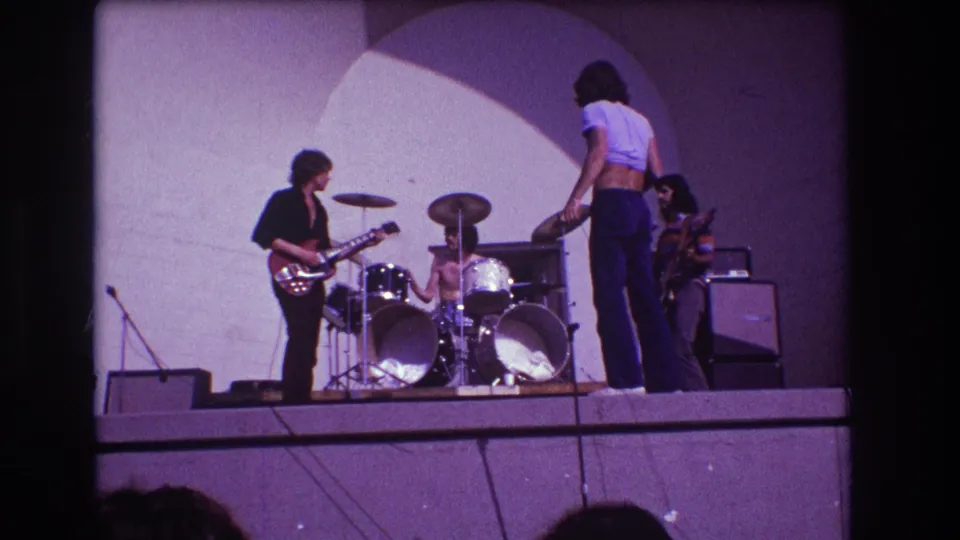 1973 Medford, New Jersey 8mm frame showing the vocalist shifting position near the drummer while the guitarist plays at left and another musician stands by equipment at right.