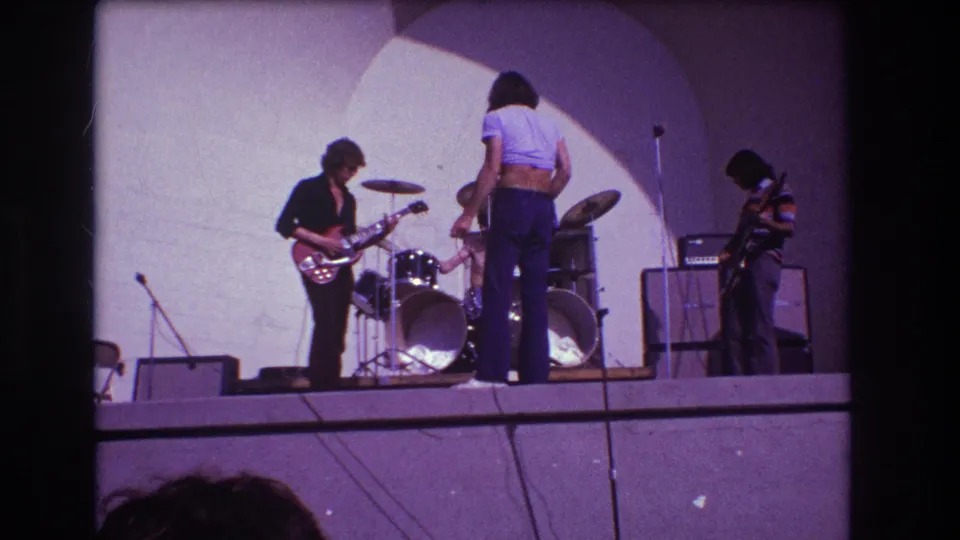 1973 Medford, New Jersey 8mm frame showing the vocalist turned toward the drummer, with guitarist at left and a musician near amplifiers at right.