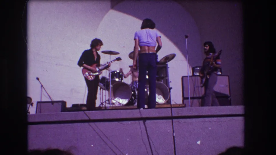 1973 Medford, New Jersey rock performance frame with vocalist centered in front of the drum kit, guitarist at left, and another musician by the amplifiers.