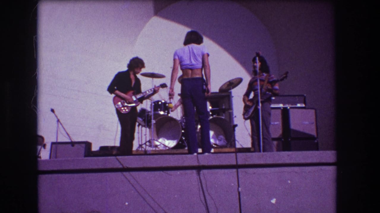 Three musicians on stage with drum kit, guitars, amplifiers, and dark frame borders.