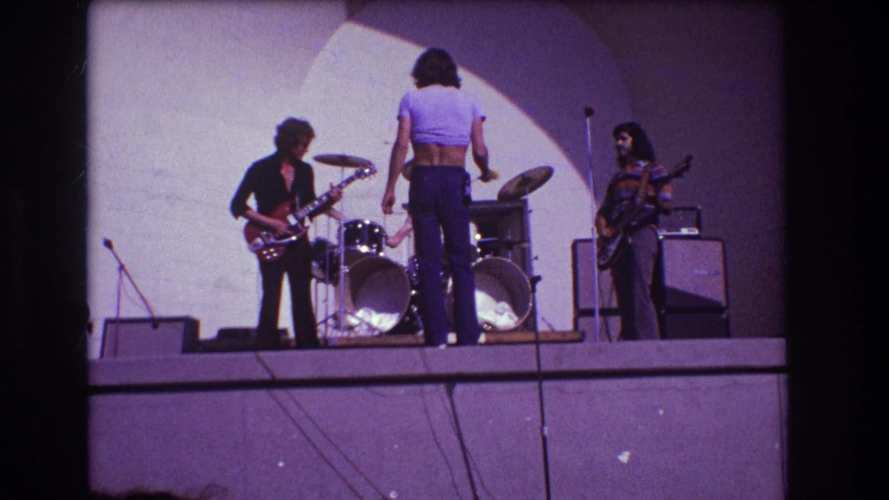 1973 Medford, New Jersey 8mm frame showing a small rock band rehearsing on stage with guitars, drums, microphones, and amplifiers.