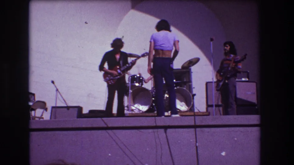 1973 Medford, New Jersey 8mm still showing guitarists, a front performer in a crop top, and a drummer on a small stage.