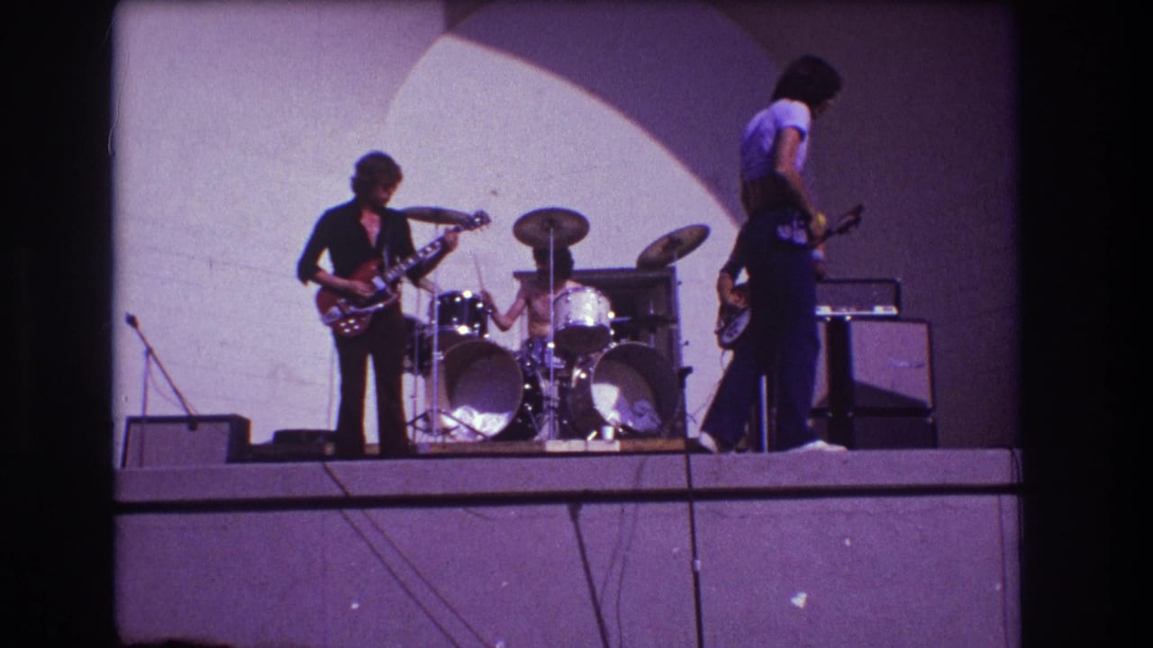 1973 Medford, New Jersey 8mm frame of a small rock band mid-performance with guitars, drums, microphones, and stage equipment.