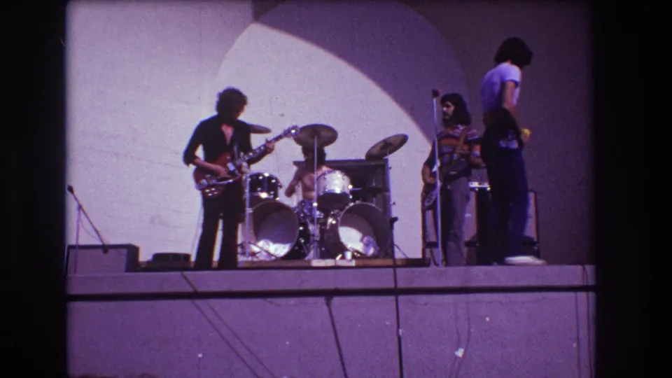 1973 Medford, New Jersey home-movie frame showing band members arranged across an outdoor stage during a live performance.