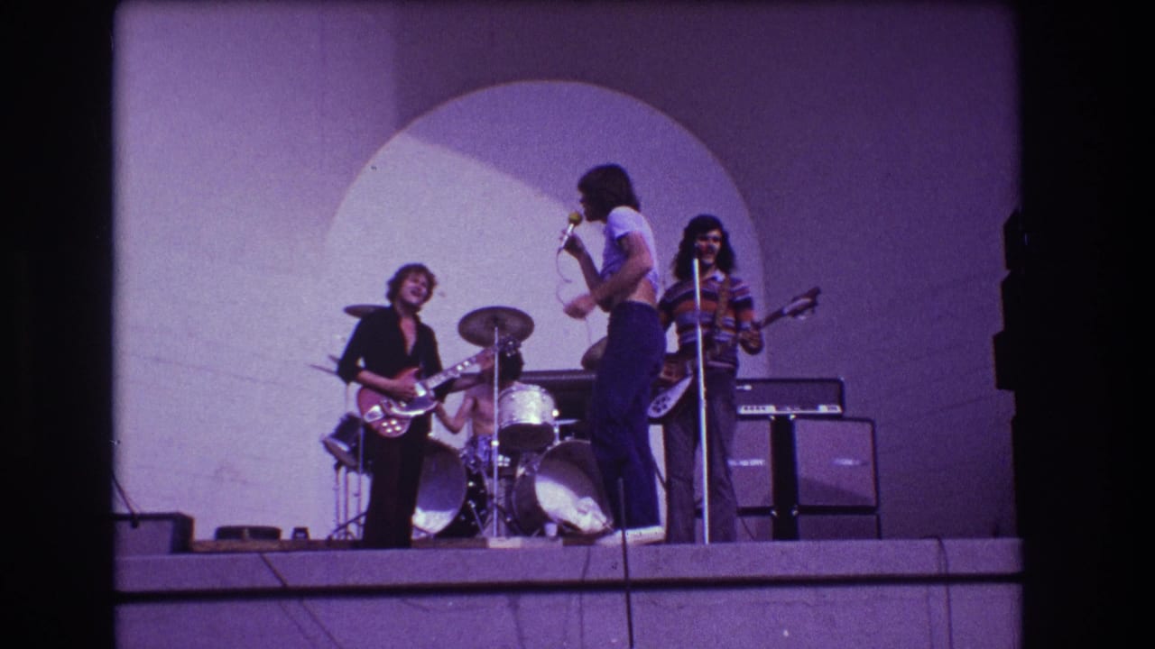 Outdoor stage with rock band performing under a circular backdrop.