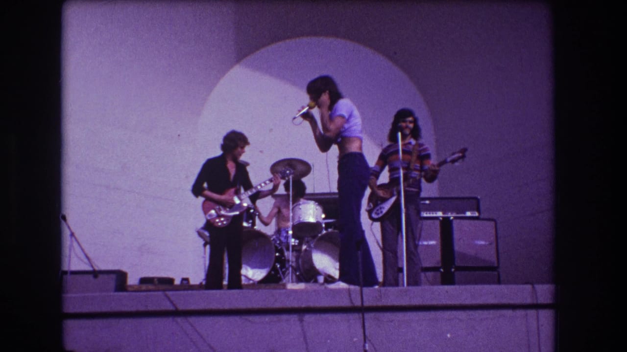 Singer leans toward a microphone as band members play behind him.