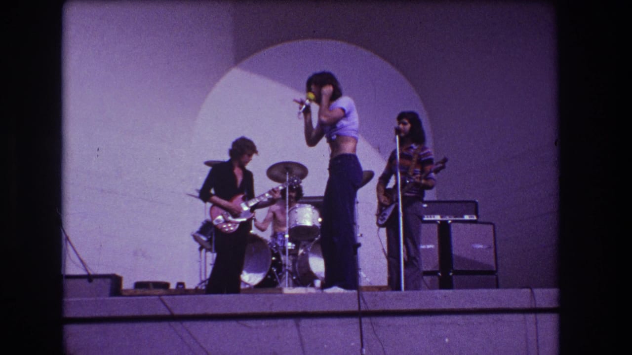 1973 Medford, New Jersey 8mm frame showing a female singer at a microphone with guitarist, drummer, and bassist on a purple-lit stage.