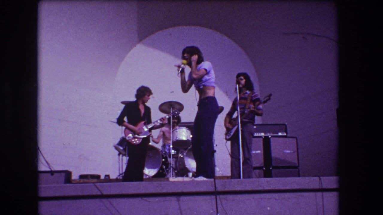 1973 Medford, New Jersey concert frame with a singer at the microphone, guitarist at left, drummer behind, and bassist near amplifiers.