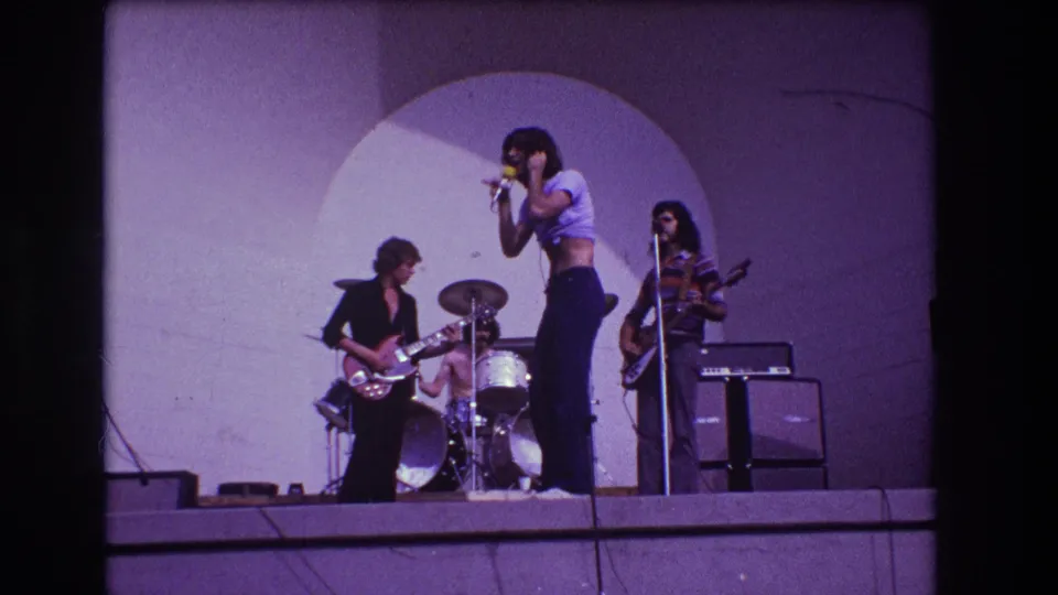1973 Medford, New Jersey concert frame with a singer at the microphone, guitarist at left, drummer behind, and bassist near amplifiers.