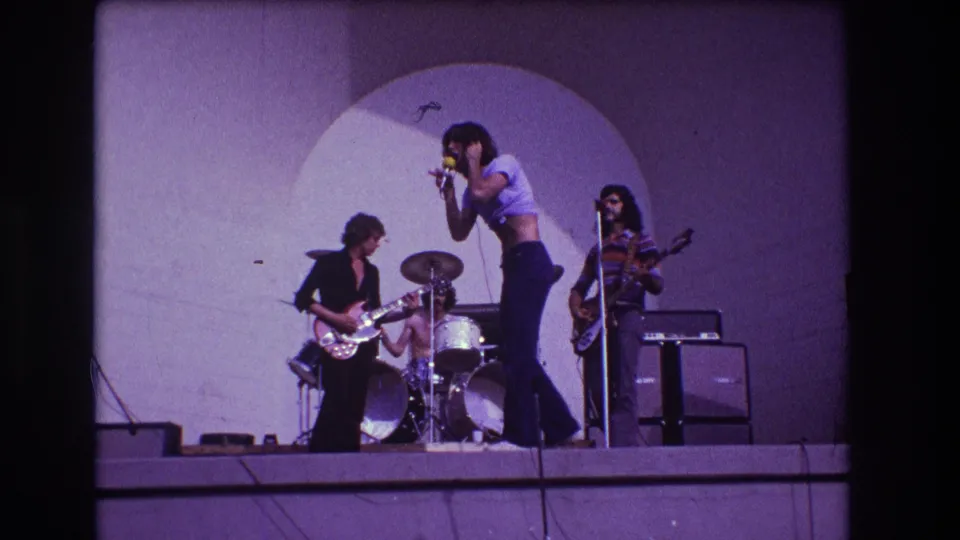 1973 Medford, New Jersey 8mm still of a rock singer performing near a microphone with guitarist, drummer, bassist, and stage amplifiers.