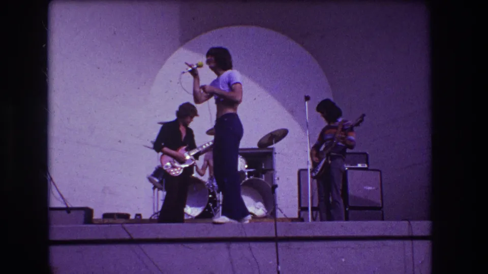 1973 Medford, New Jersey home-movie frame of the band mid-performance, with the singer centered and musicians arranged around the drum kit.