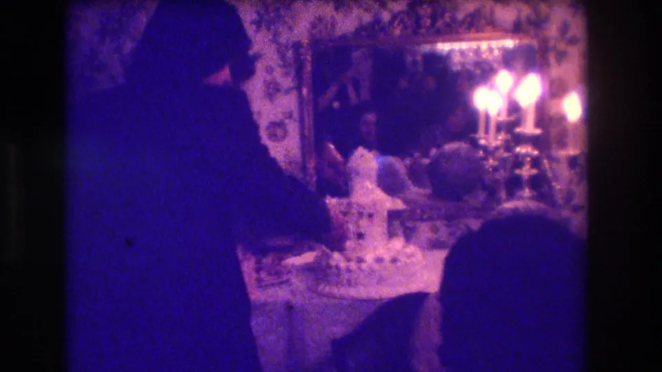 Brief home-movie cutaway or transition frame with dark silhouettes and bright candle-like lights, likely separate from the outdoor stage view.