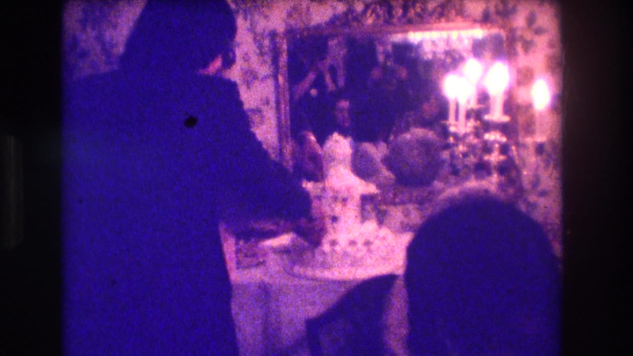Couple beside a white wedding cake in a dim ornate room with mirror and candles.