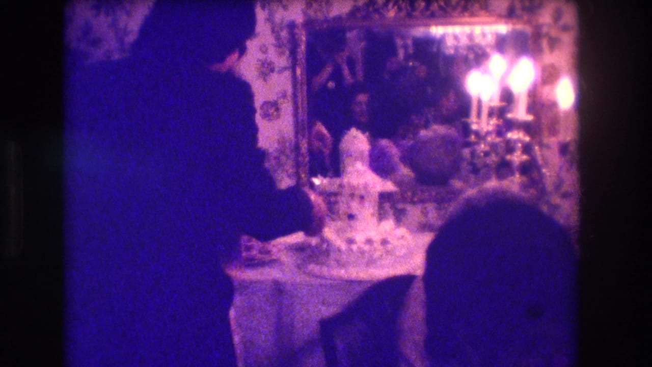 Silhouetted couple at a wedding cake table with mirror, candles, and floral wallpaper.
