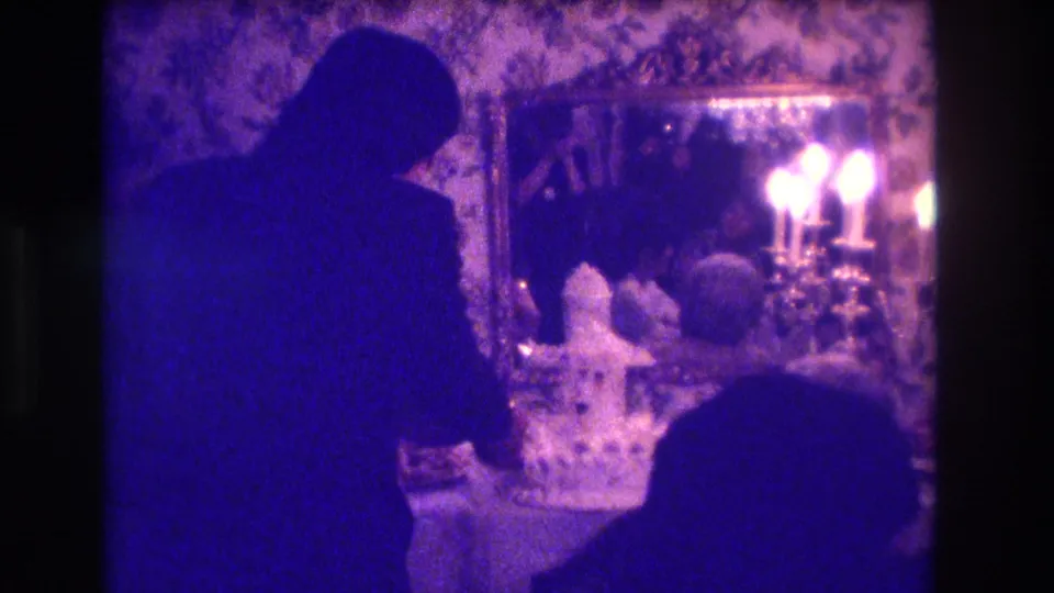 A dim 1973 Medford wedding reception frame shows the couple near the cake table, with candlelight reflected in a large mirror.