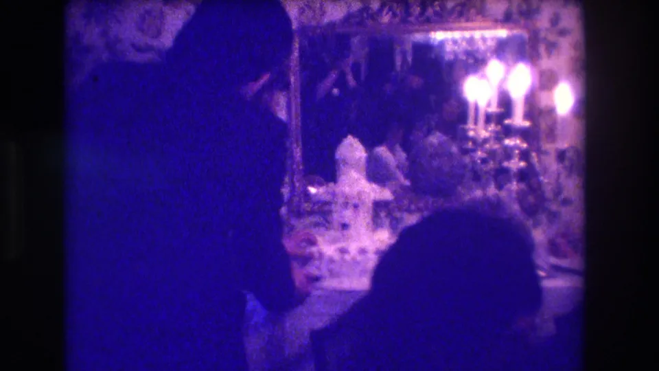 1973 Medford, New Jersey 8mm frame showing a wedding figure leaning toward the cake table in a dim room with candles and an ornate mirror.