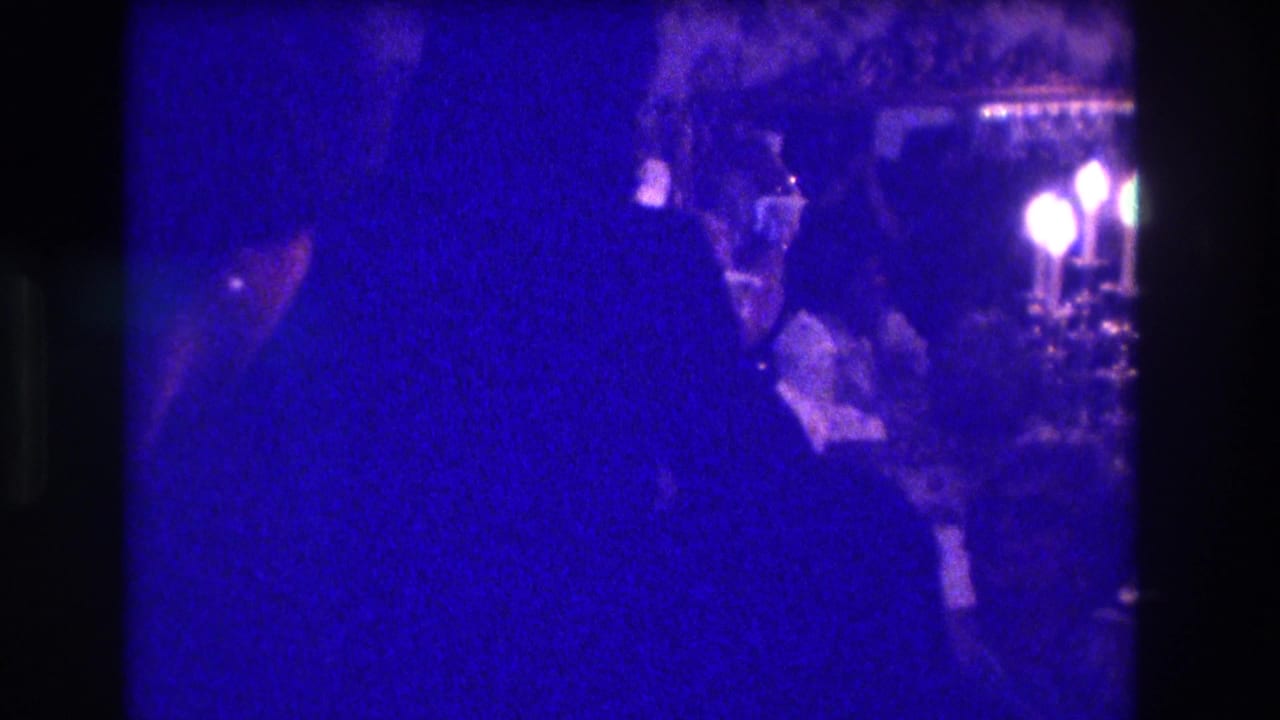 Silhouetted woman dancing in a dim room with candlelight and seated viewers behind her.