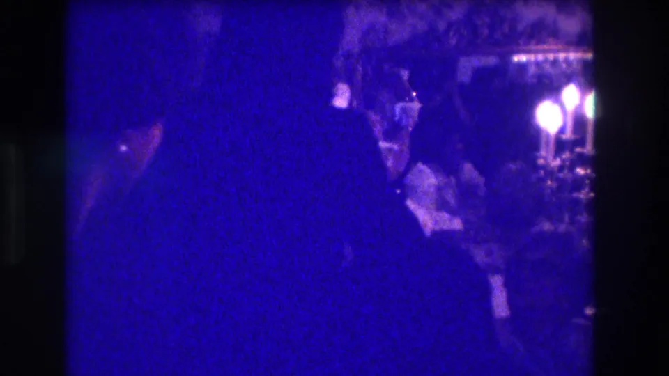 1973 Medford home-movie frame showing a silhouetted woman dancing in a dim indoor room with candlelight and seated viewers.