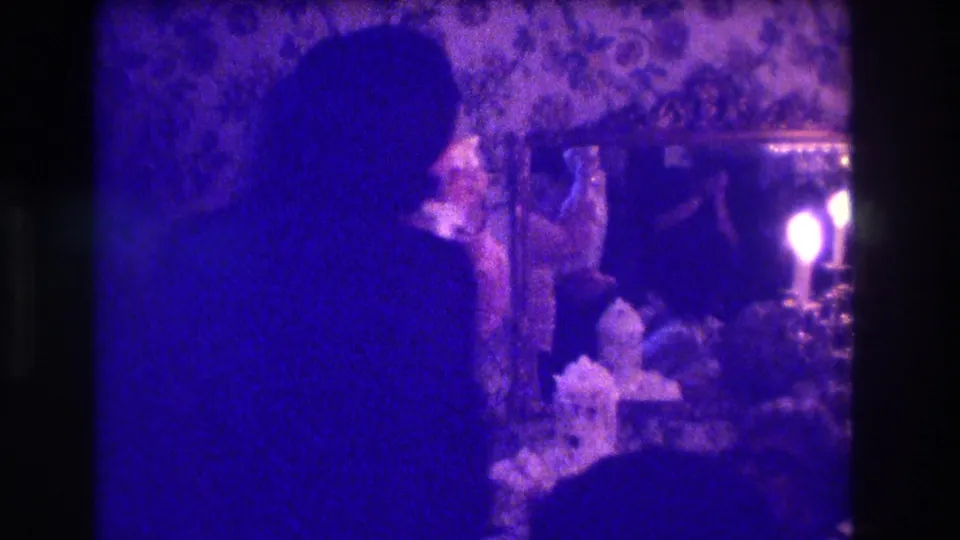 1973 Medford home-movie frame showing a woman in profile dancing near floral wallpaper and a candlelit table.