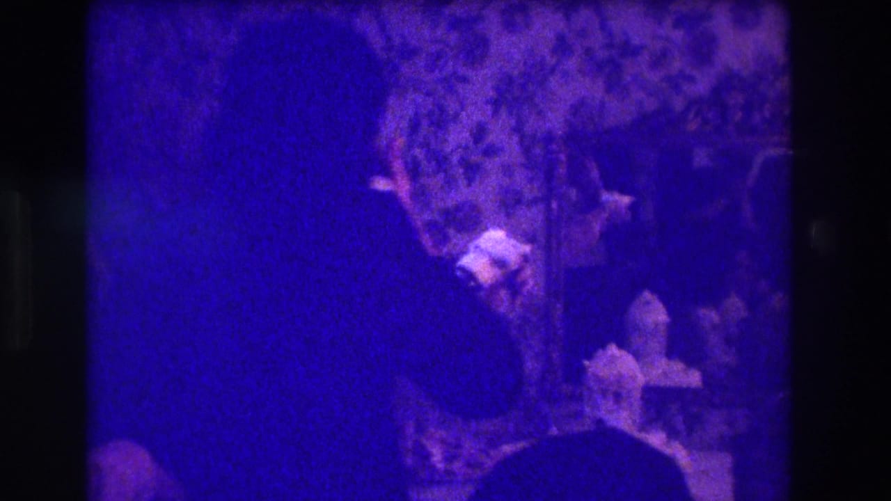Dark purple-tinted frame with a woman in silhouette near a table and decorated dessert.