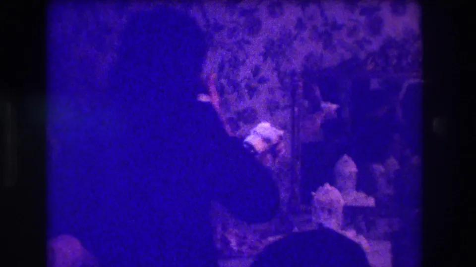 1973 Medford home-movie frame showing a silhouetted woman near a table with a cake-like object in a dark private room.