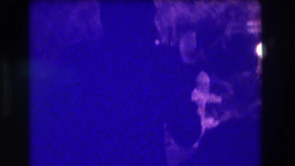 A grainy 1973 Medford interior frame shows a partially visible person beside a table with small objects and a possible dessert.