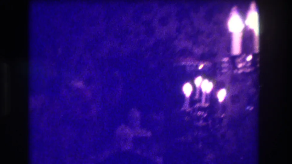 Final 1973 Medford frame shows candle flames and faint seated or standing figures under strong purple low-light film cast.