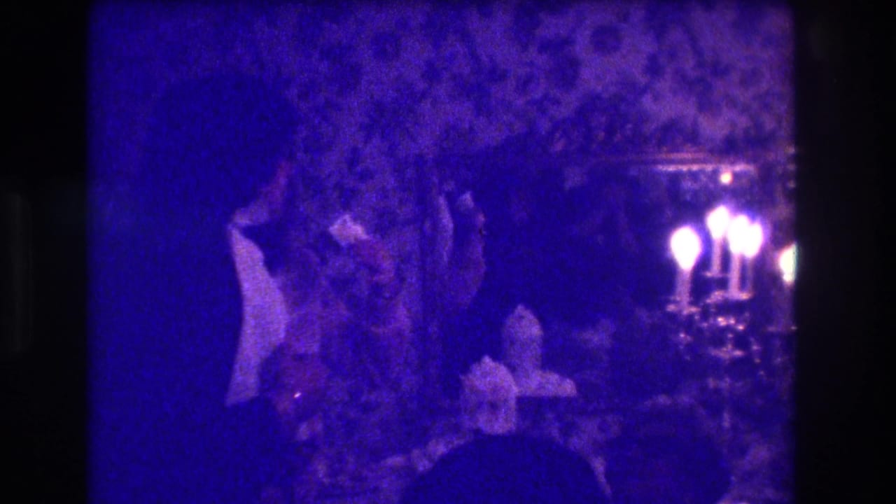 1973 Medford, New Jersey 8mm frame showing adults in formal attire gathered in a dim room with floral wallpaper and candlelight.