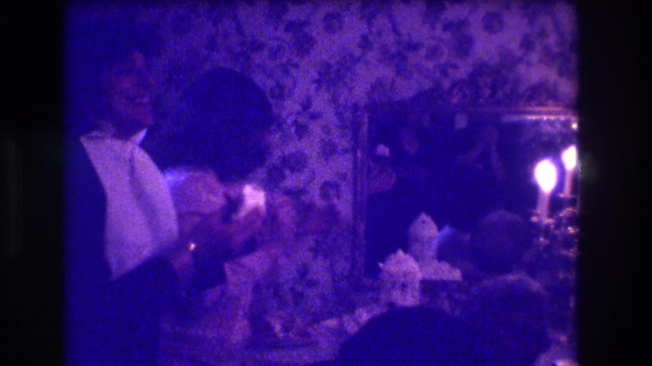 Tuxedoed man leans toward a seated woman at an indoor wedding party.