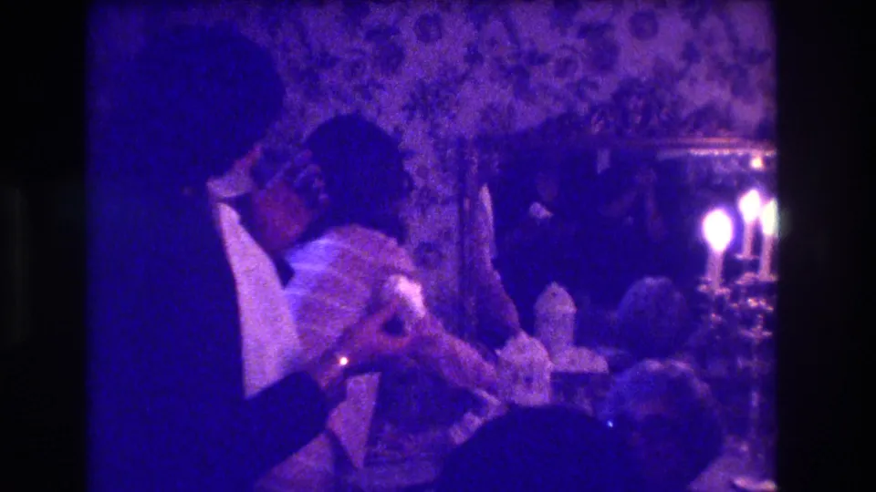 A candid 1970s wedding-party frame shows the seated woman lowering her head while the tuxedoed man remains close by.